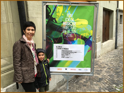 Yuuko Suzuki standing beside the Fête de la Musique Fribourg 2016 street poster listing the Centre le Phénix stage
