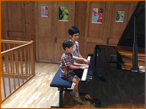 Two children sitting together at the grand piano in the wood-panelled hall at Centre le Phénix