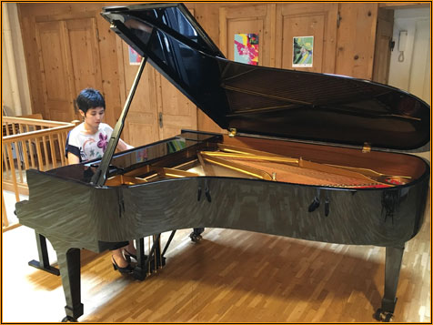 The open grand piano in the wood-panelled hall at Centre le Phénix, a child seated at the keyboard